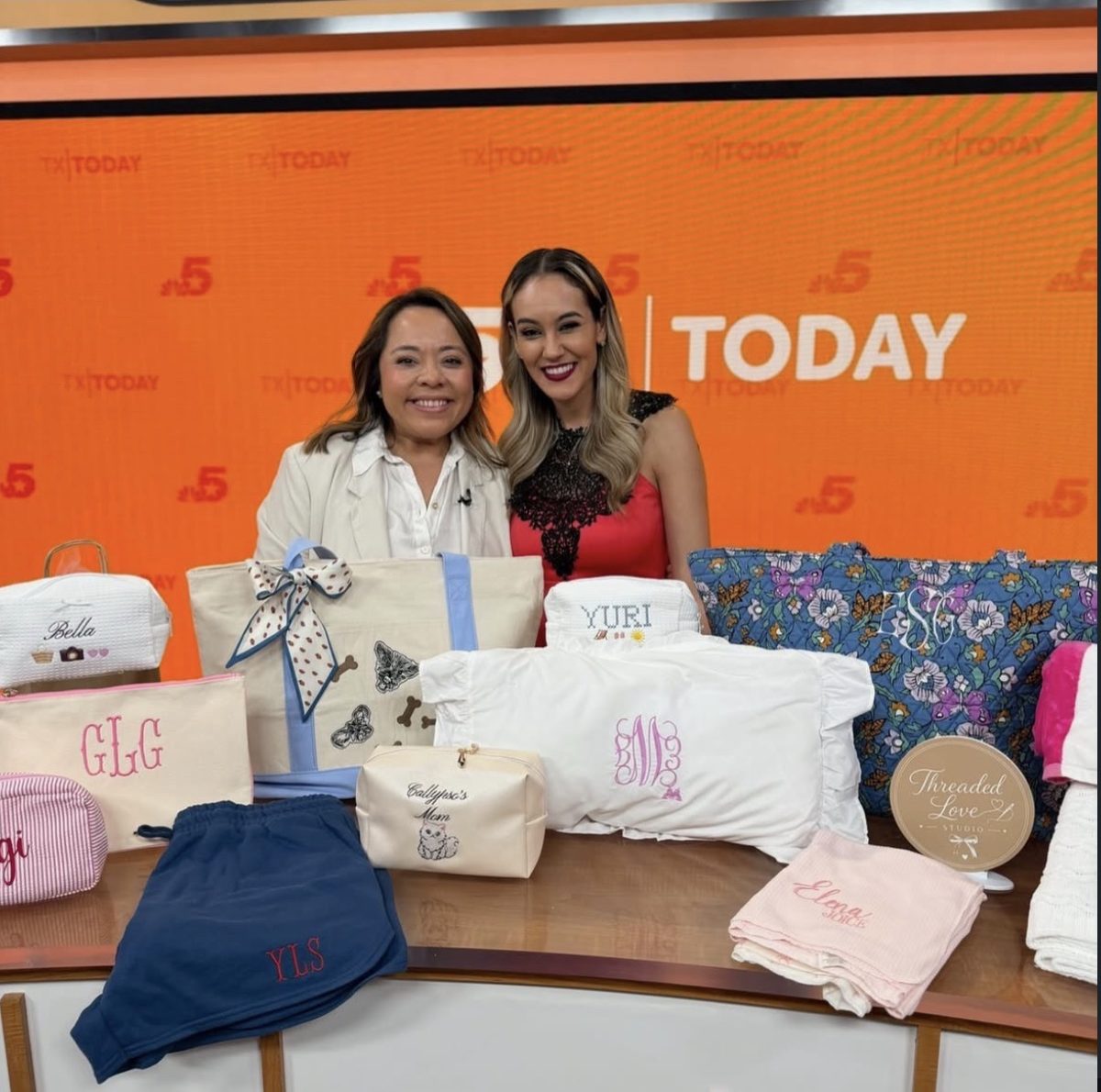 Yuri of Threaded Love Studio on the NBC 5 Texas Today set with anchor Adriana Lopez and a table of personalized embroidered pieces